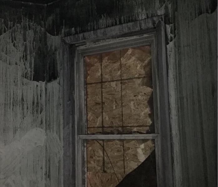 A room with walls covered in soot with a boarded up window.