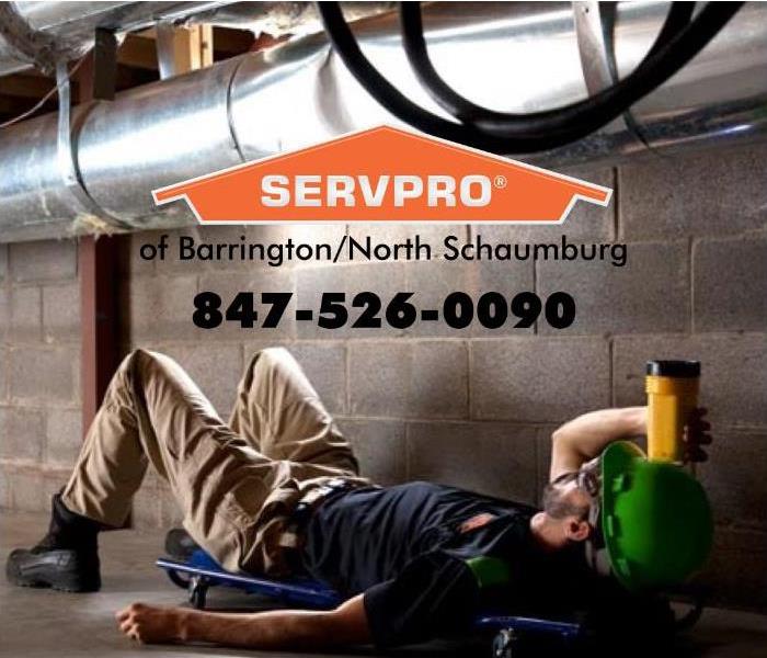 SERVPRO employee laying down with a yellow flashlight looking at a silver furnace pipe.