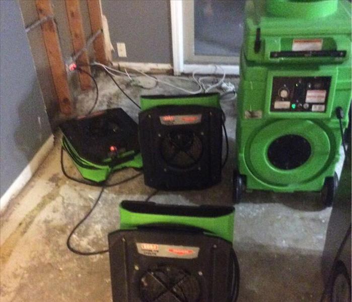 Green dehumidifier and three air blowers set up on a kitchen floor.